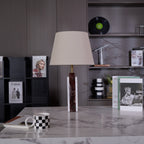 A Clérachic table lamp lit on a stone plinth, a magazine and checkerboard mug arranged beside its dark veined base.