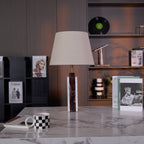Clérachic's marble table lamp glows on a stone side table, a book stack and dried flower stem set against a dark shelf.