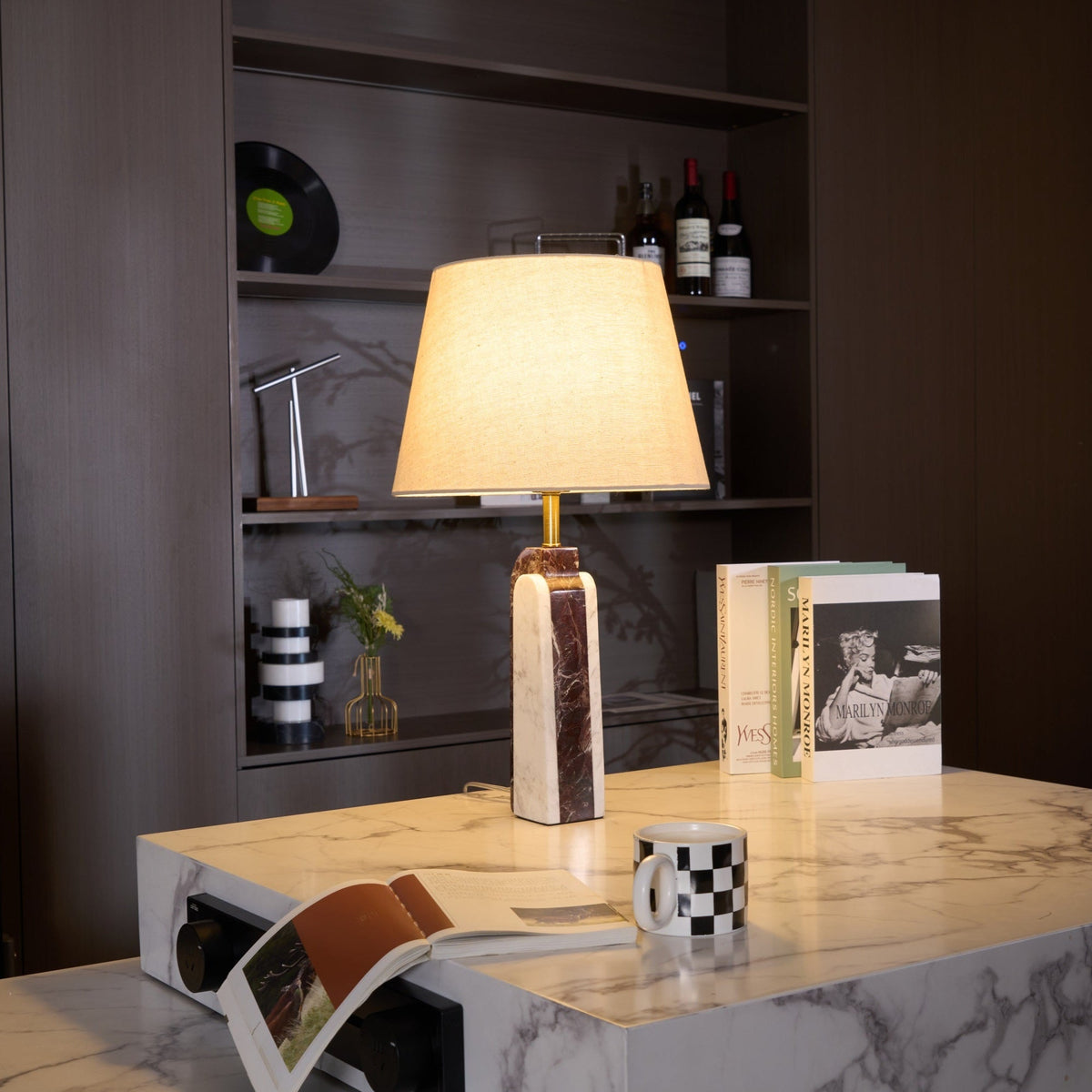 A Clérachic marble table lamp lit beside a checkerboard mug on a stone plinth, vinyl records visible on the shelf behind.