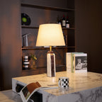 Clérachic's marble table lamp glows on a stone side table, a small desk lamp and stacked books on the shelf behind.