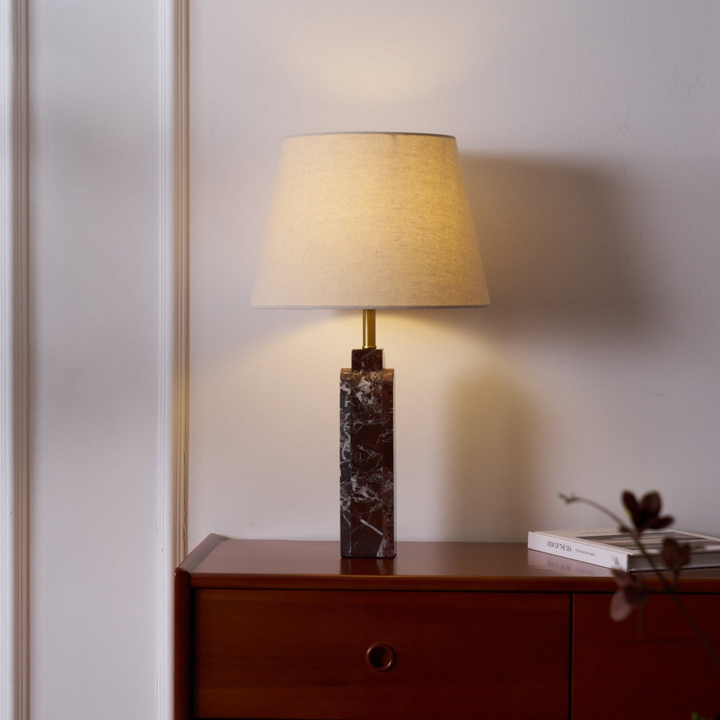 Clérachic's marble table lamp glows on a walnut dresser, a dried flower sprig and book set beside its stone column.