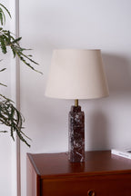 A cropped view of the Clérachic table lamp lit on a dresser, a potted plant visible at the edge of the frame.
