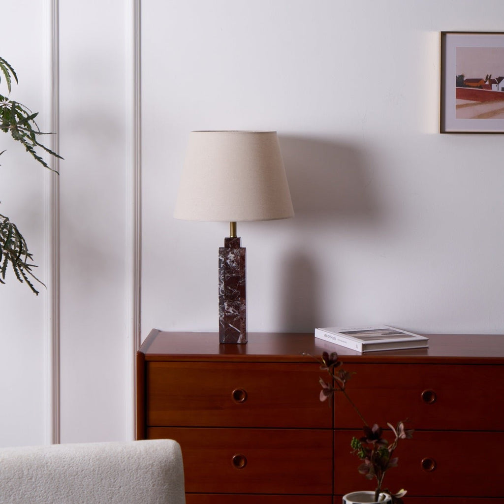 This Clérachic table lamp sits unlit on a walnut dresser, a small vase of dried flowers in the background.