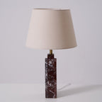 A Clérachic marble table lamp lit on a studio background, the beige shade glowing above its dark veined column.