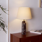A Clérachic dark purple marble table lamp glows on a walnut dresser, its beige linen shade warming the white panelled wall.
