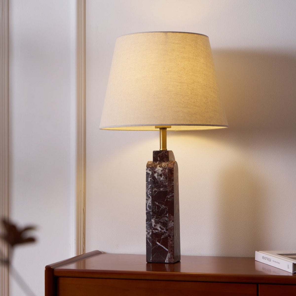 The Clérachic marble table lamp lit on a walnut dresser, warm light spilling across the white panelled wall.