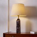 This Clérachic marble table lamp sits lit on a dresser, its brass neck catching light beneath the tapered fabric shade.