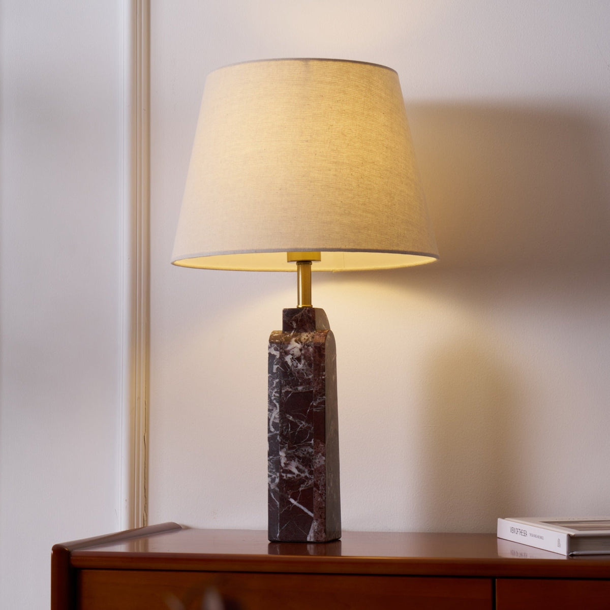 This Clérachic marble table lamp sits lit on a dresser, its brass neck catching light beneath the tapered fabric shade.
