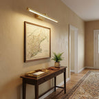 Warm light from this Clérachic wall light in brass falls across a framed map on a beige hallway wall.