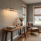 In a pale grey hallway, this Clérachic wall light in brass sits above a wooden console table and armchair.
