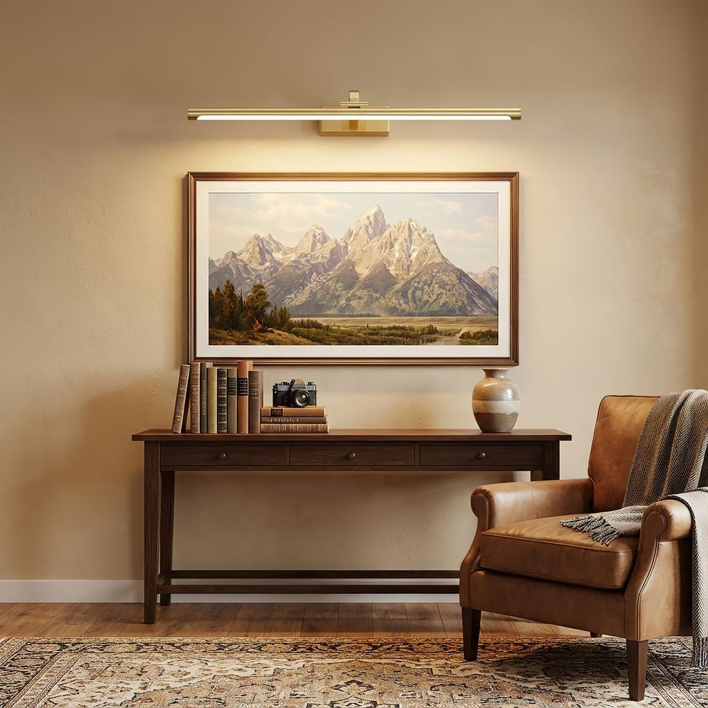 Mounted over a mountain print, this Clérachic wall light in brass lights a dark wood console table with books.