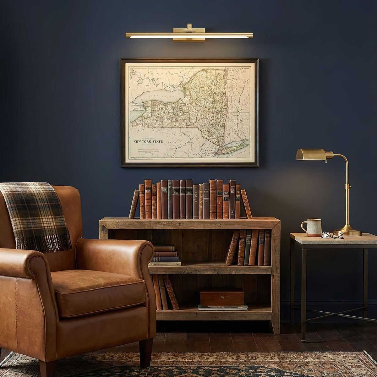 Brass finish on this Clérachic wall light throws warm light over a framed map in a navy blue living room.