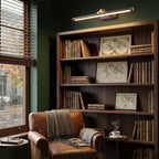 Mounted above a dark wood bookshelf lined with vintage maps, this Clérachic wall light in brass warms a green-walled reading nook.