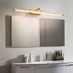 Mirrored cabinet doors sit below this Clérachic wall light in brass, lit, over a white bathroom counter.