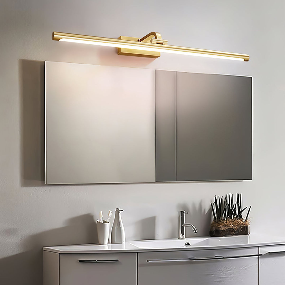 Mirrored cabinet doors sit below this Clérachic wall light in brass, lit, over a white bathroom counter.