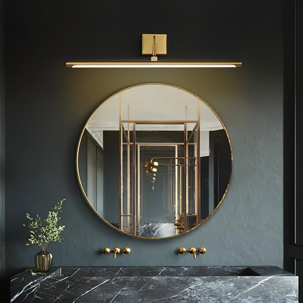 A round mirror in a dark green marble bathroom sits beneath this Clérachic wall light in brass.