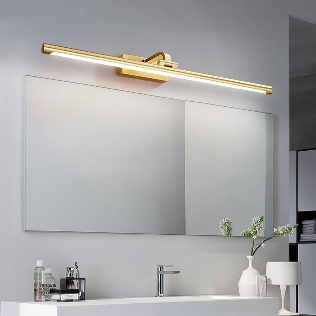 Fresh flowers stand beside a white vanity beneath this Clérachic wall light in brass, above a wide mirror.