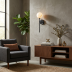 This black Clérachic wall sconce glows on a plaster wall above a grey armchair and a wood credenza.