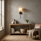 This black Clérachic wall sconce lights a plaster wall above a console table and a leather chair.