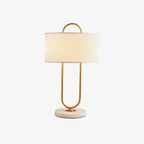 Lit against a plain white backdrop, this Clérachic table lamp shows its full white linen shade glowing above the looped brass frame.