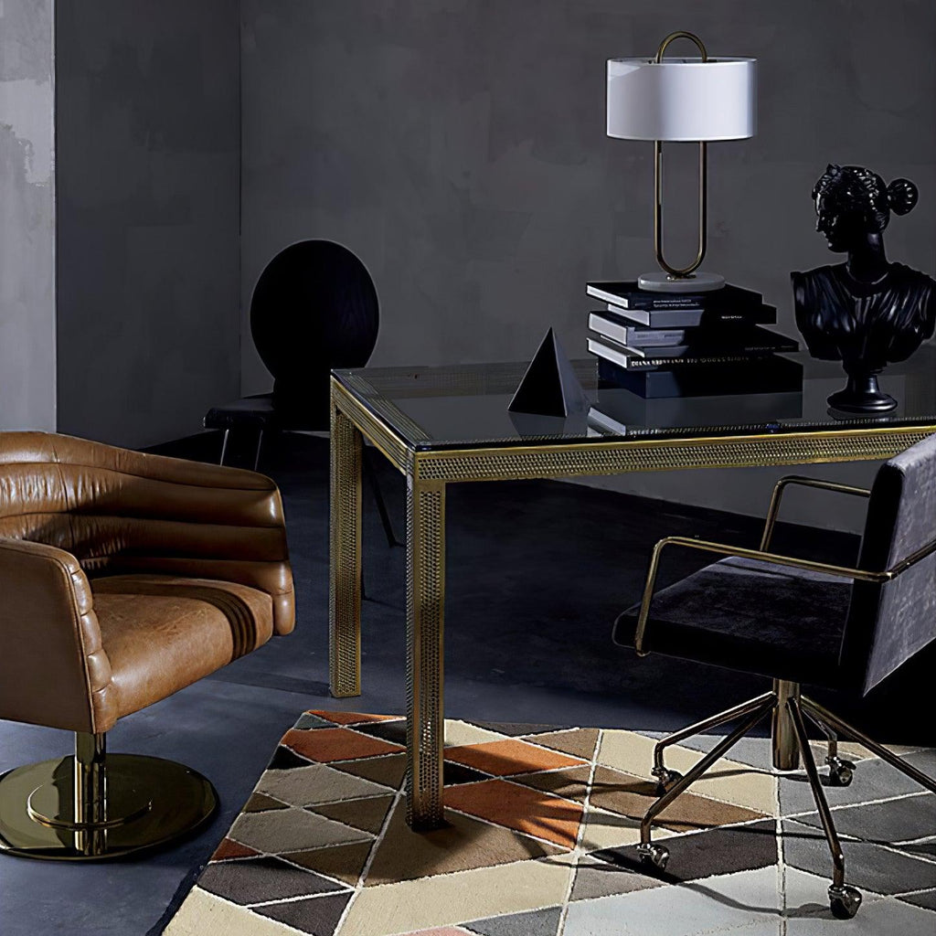Seen in the background of a dark, moody room, this Clérachic table lamp stands on a glass desk beside a black bust and stacked books.