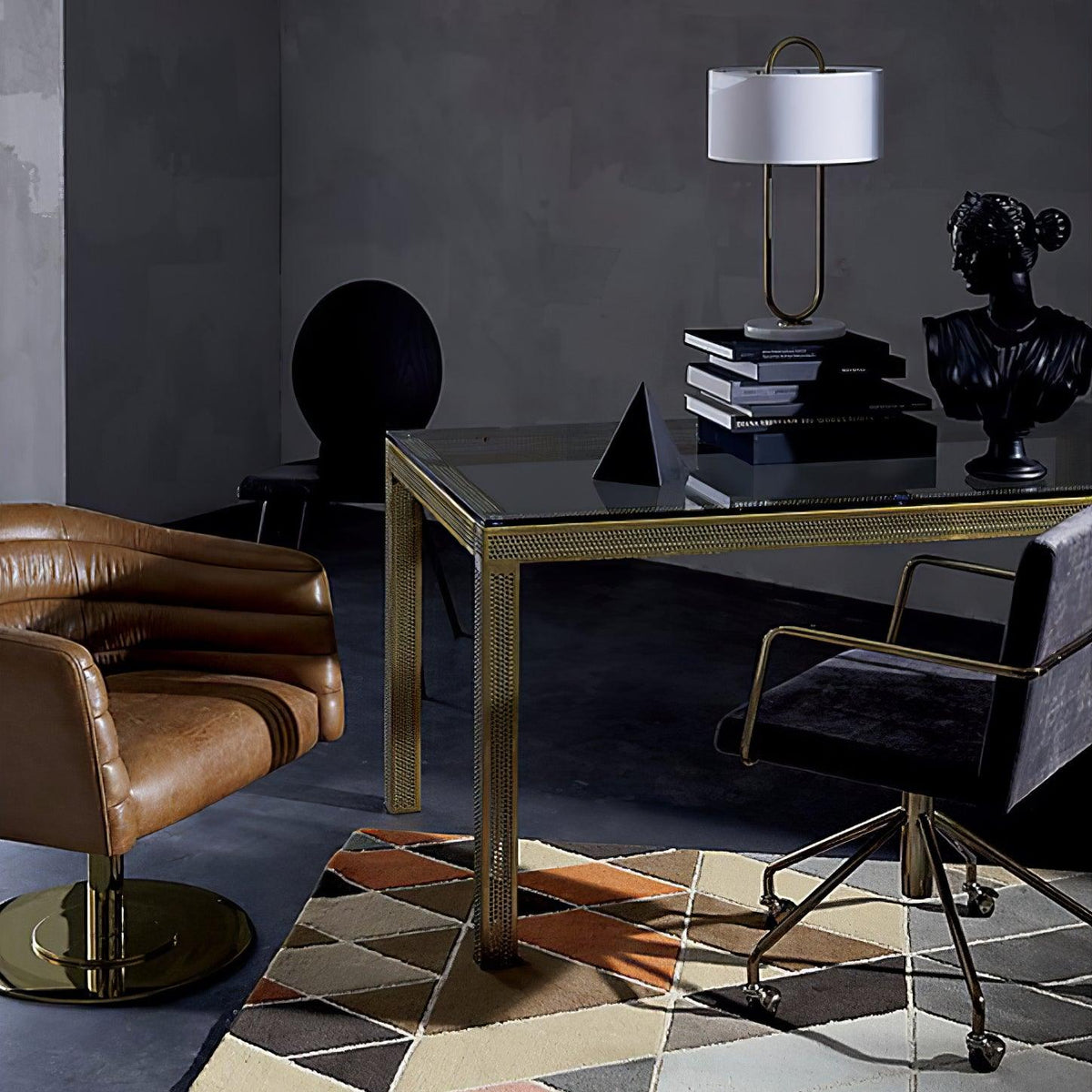 Seen in the background of a dark, moody room, this Clérachic table lamp stands on a glass desk beside a black bust and stacked books.