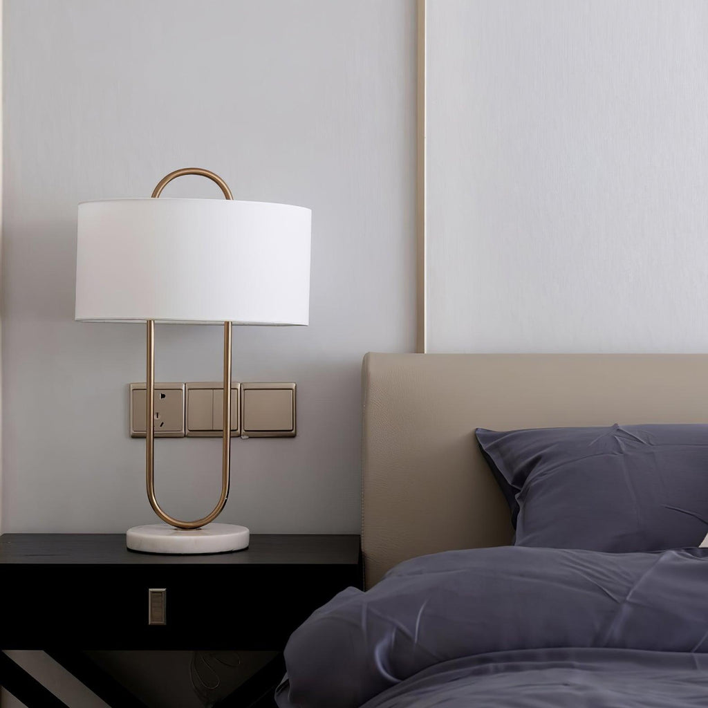 Beside a taupe headboard and navy bedding, this Clérachic table lamp's gold frame stands close to a wall switch plate on the nightstand.