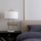Beside a taupe headboard and navy bedding, this Clérachic table lamp's gold frame stands close to a wall switch plate on the nightstand.