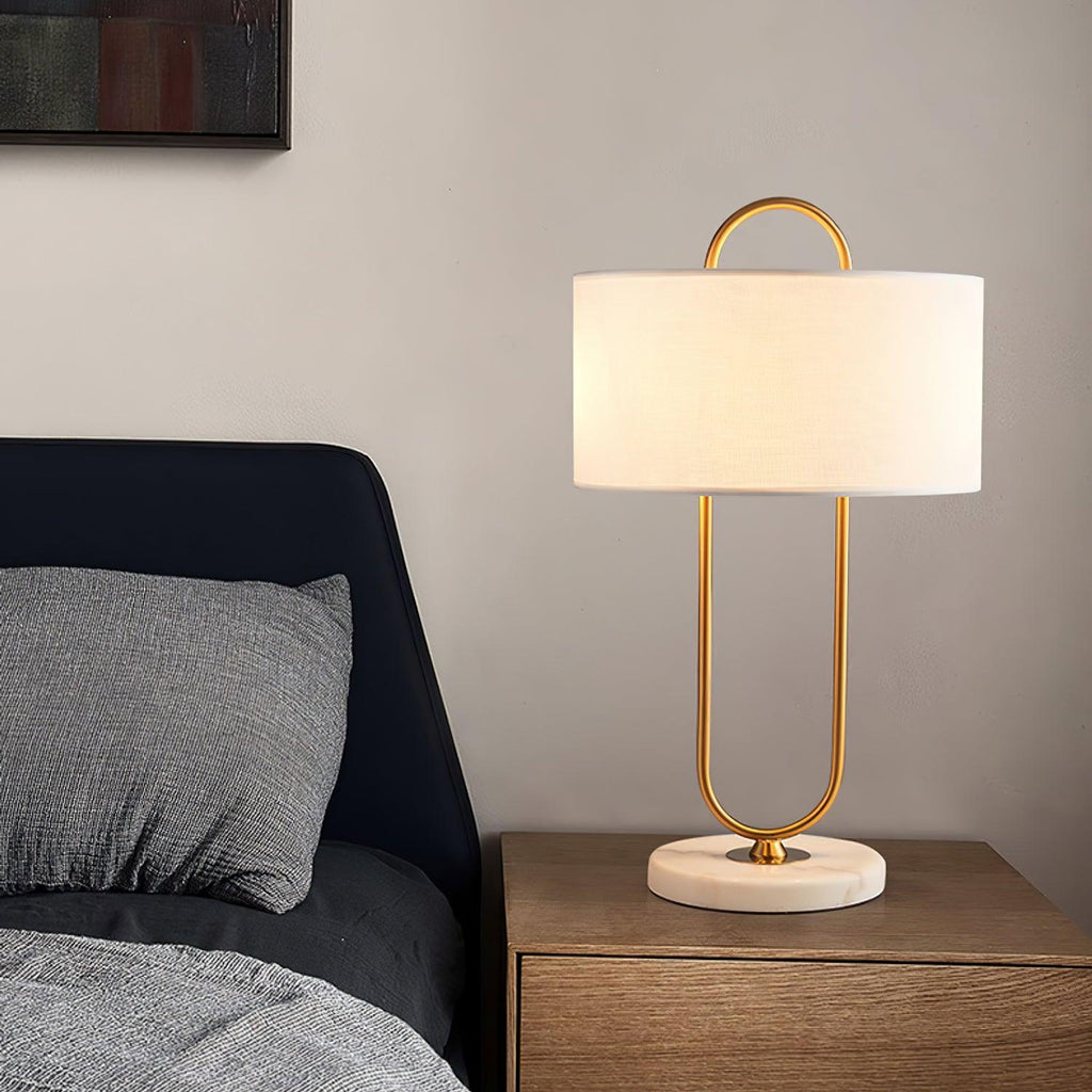 Next to a black leather headboard, this Clérachic table lamp's curved brass frame rises from a round marble base on a wood nightstand.