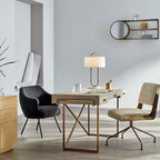 In a home office, this Clérachic table lamp sits on a gold-framed desk beside an armchair and a low bookshelf against a plain wall.