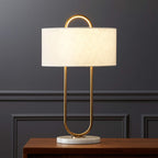 This Clérachic table lamp sits on a wood nightstand against a dark charcoal panelled wall, its brass loop frame rising from a round marble base.