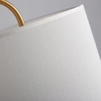 A close-up shows the woven linen texture of this Clérachic lamp's shade edge where it meets the curved brass frame.