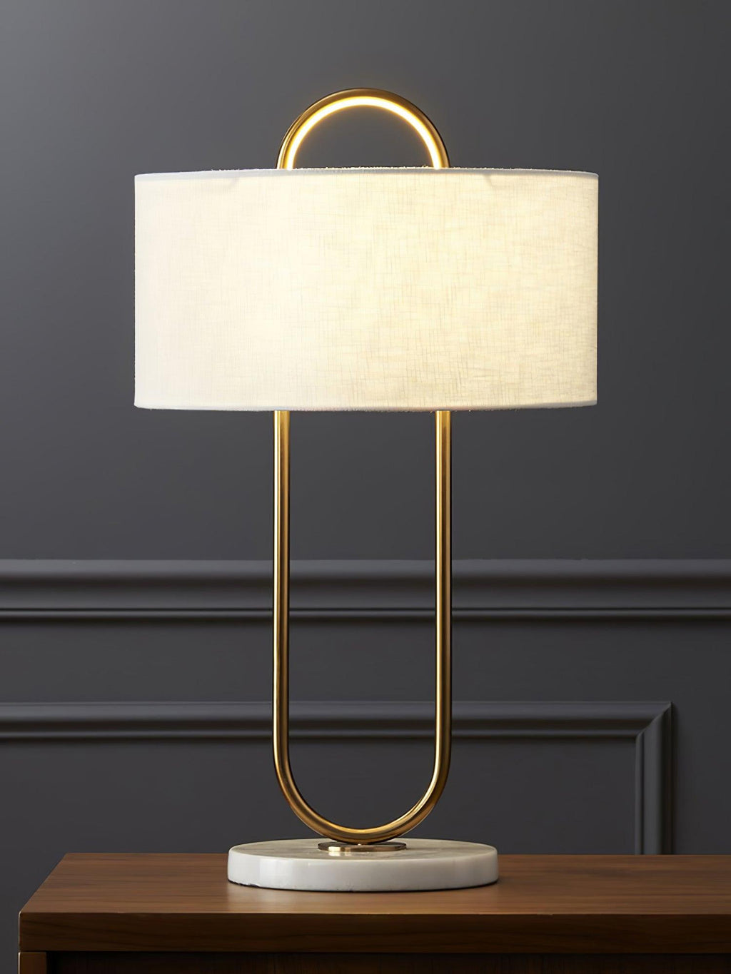 On a wood nightstand against a dark panelled wall, this Clérachic table lamp's unlit linen shade sits above its curved brass stem.