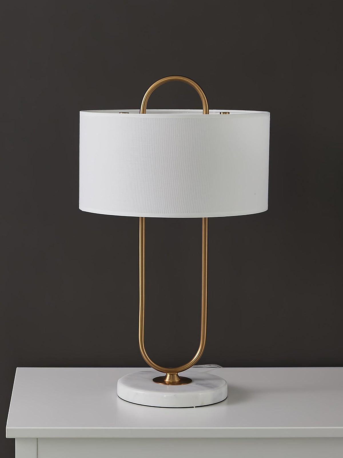 Photographed on a white dresser top against a dark charcoal backdrop, this Clérachic table lamp's marble base and brass frame stand out.