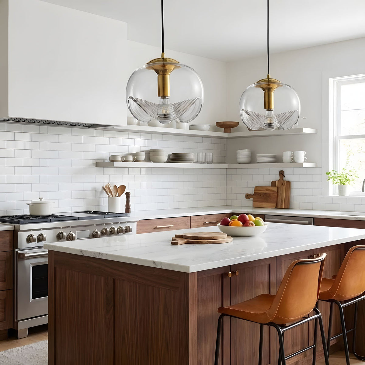 Two clear glass pendants with gold frames hang above a dark wood kitchen island with white countertops and leather bar stools, this Clérachic light shown in a pair.