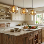 Three amber glass shades with gold frames hang in a row above a rustic wood-and-white kitchen island, this Clérachic fixture shown as a triple cluster.