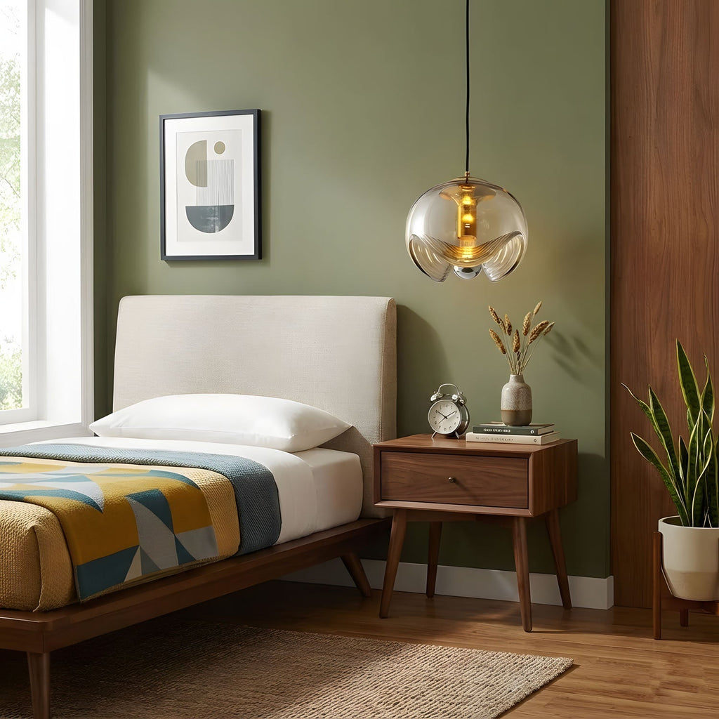 Against an olive-green wall above a wooden bed, this Clérachic pendant's amber glass shade and gold frame hang beside a framed abstract print.