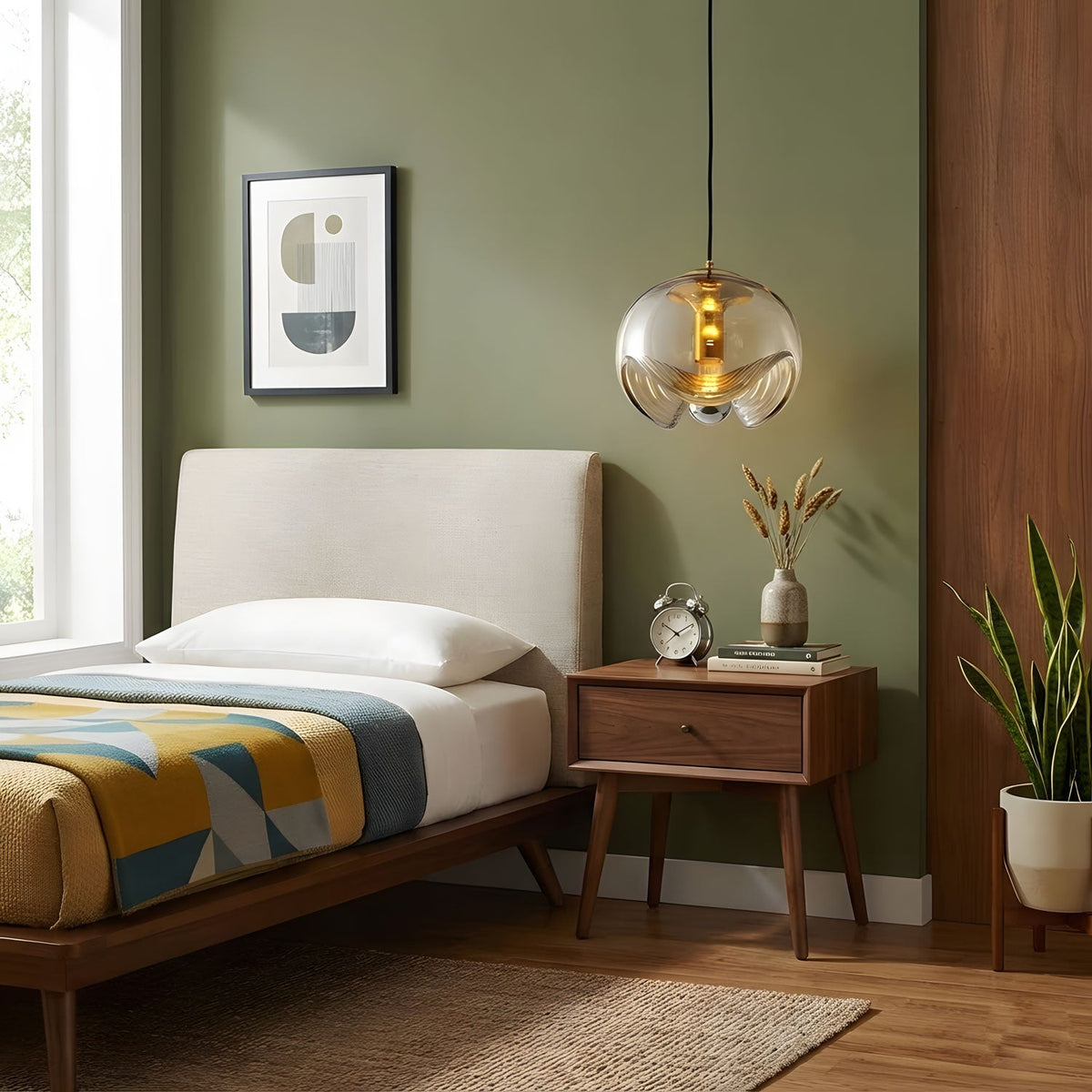 Against an olive-green wall above a wooden bed, this Clérachic pendant's amber glass shade and gold frame hang beside a framed abstract print.