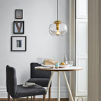 In a small dining nook with framed black-and-white prints, this Clérachic pendant's clear glass shade and gold frame glows above a round table.