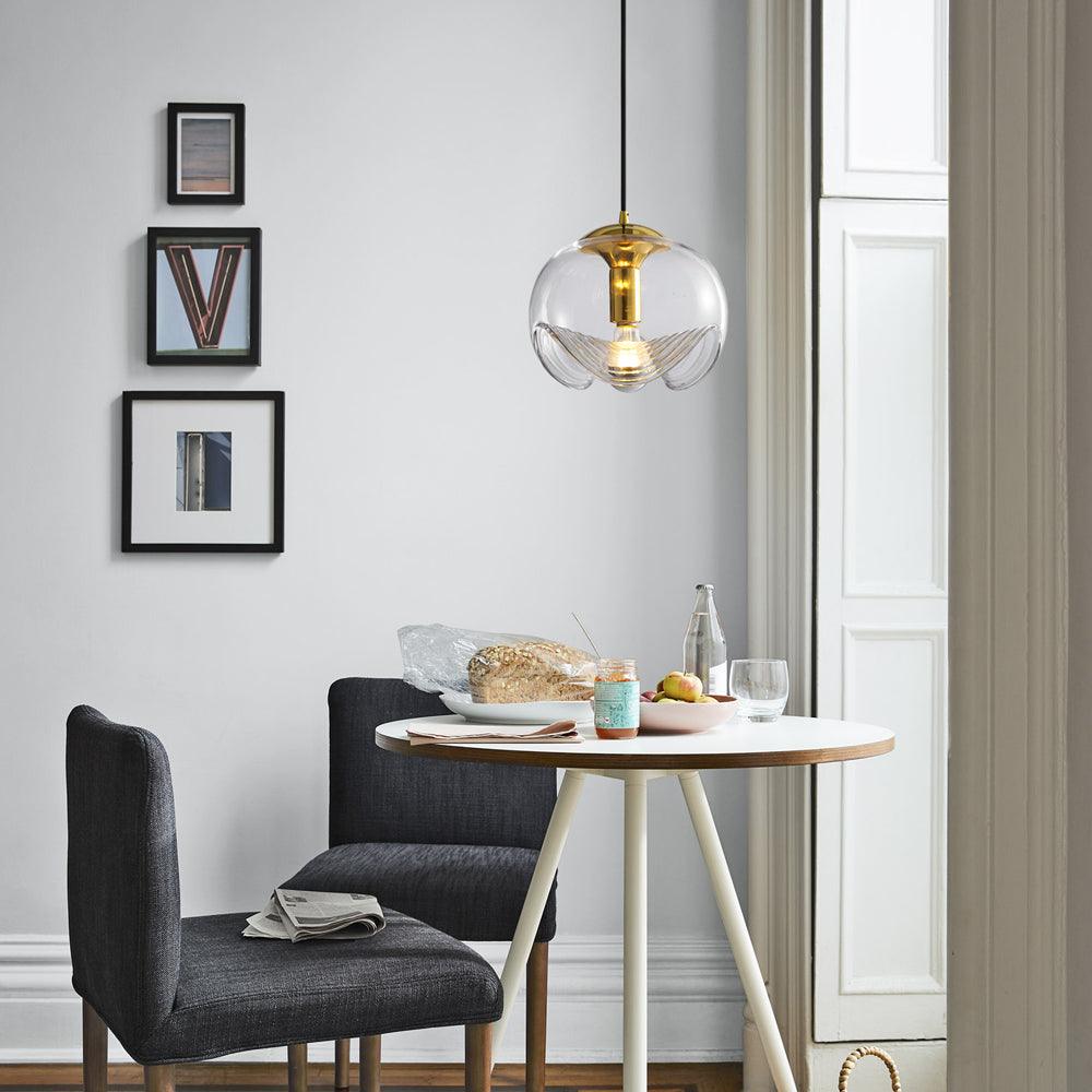In a small dining nook with framed black-and-white prints, this Clérachic pendant's clear glass shade and gold frame glows above a round table.