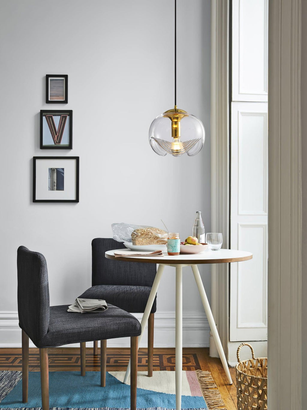 In a narrow dining corner near a doorway, this Clérachic pendant's clear glass shade and gold frame hang above a round wooden table.