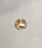 Viewed from below on a white cord, this Clérachic pendant's amber glass shade glows warmly against a plain grey background.