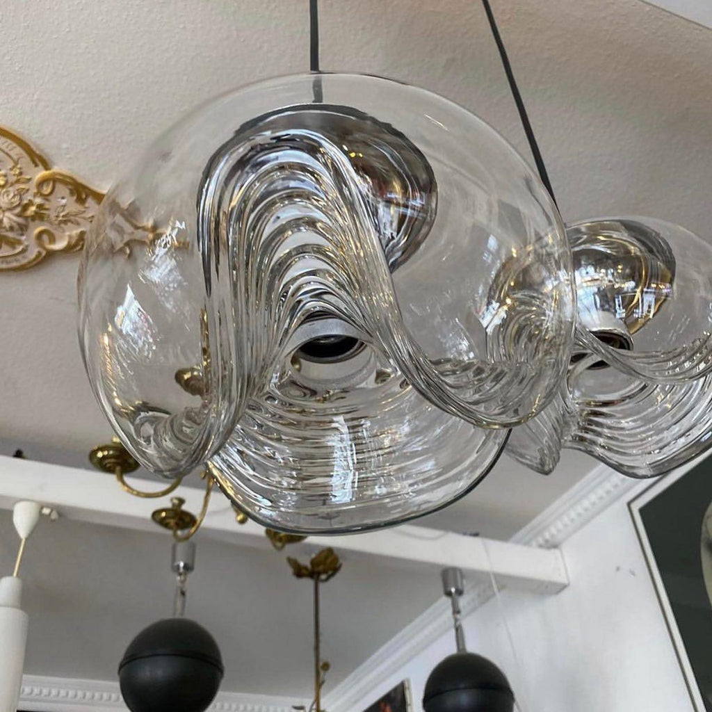 Viewed from below in a room with an ornate mirror, this Clérachic pendant's clear glass shade shows its scalloped underside and brass fitter.