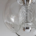 Close view of this Clérachic pendant's clear glass shade, its ribbed scalloped folds catching daylight around a chrome socket.