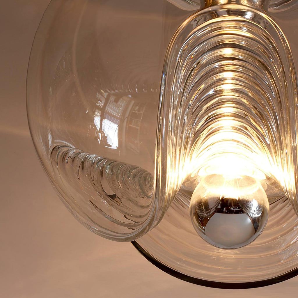 Close view of this Clérachic pendant's clear glass shade lit from within, its ribbed folds glowing warmly around a chrome socket.