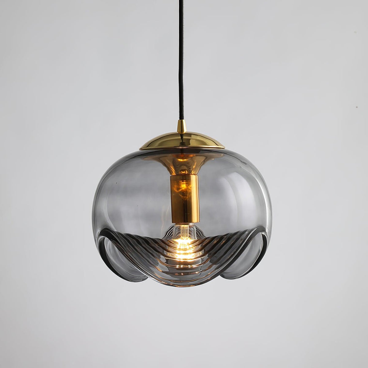 Product shot of this Clérachic pendant's smoky grey glass shade and gold frame, lit against a plain grey backdrop.