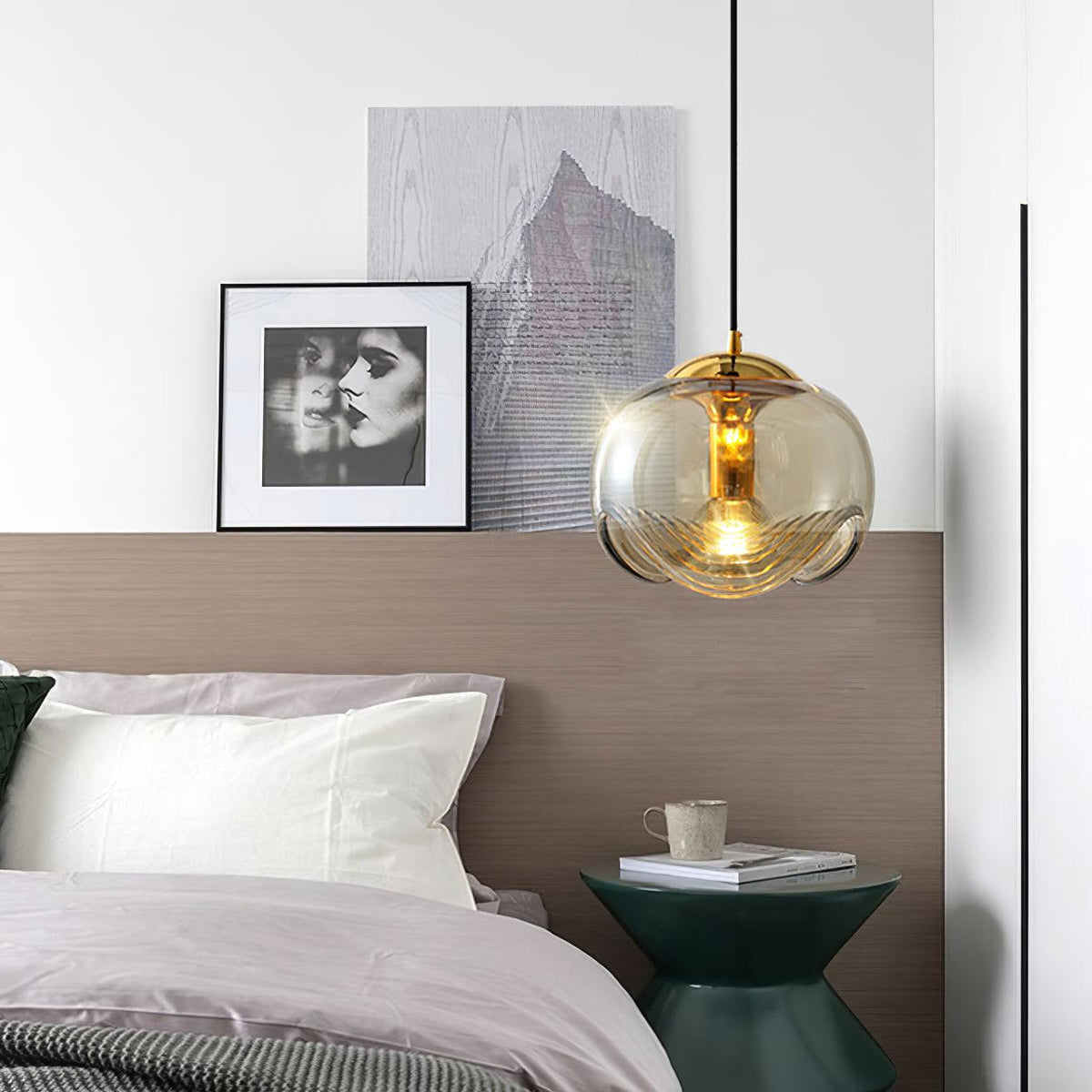 Beside a gallery of framed portraits and a floor lamp, this Clérachic pendant's amber glass shade hangs low over a bed with pink linens.