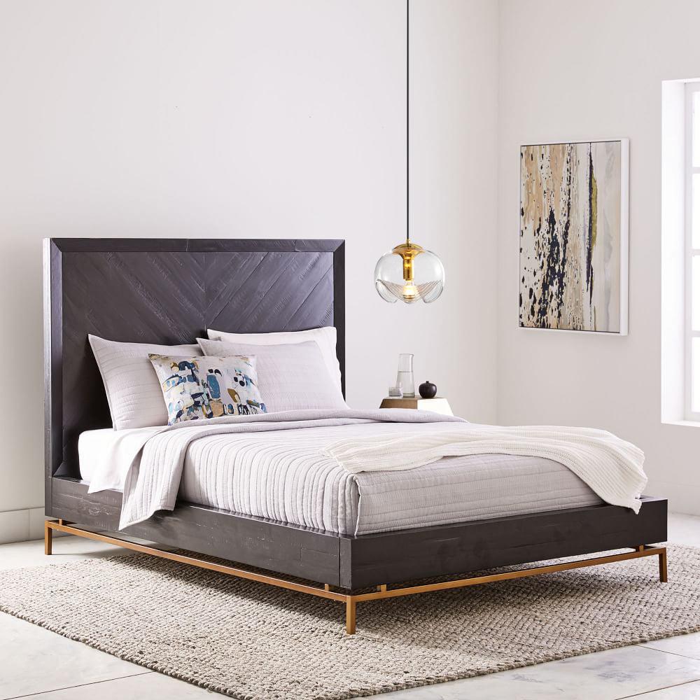 Above a charcoal upholstered bed with brass legs, this Clérachic pendant's clear glass shade and silver frame hang near a framed abstract artwork.