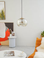 This Clérachic pendant's clear glass shade and silver frame hang above a fluted side table with fresh flowers and an orange throw pillow.