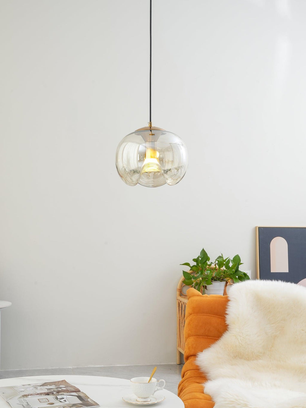 Beside a potted plant and an orange lounge chair, this Clérachic pendant's amber glass shade glows warmly against a plain white wall.